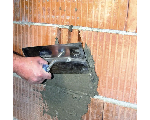 Un artisan applique du mortier sur un mur en briques à l''aide d''une truelle.