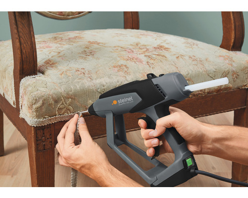 Handwerker befestigt mit einer Heißklebepistole eine Borte an einem Stuhl