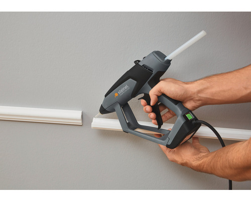 Eine Person benutzt eine Heissklebepistole von Steinel, um eine Zierleiste an der Wand zu befestigen.