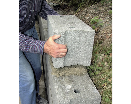Une personne pose un bloc de béton sur un mur.