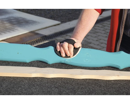 Eine Person schleift ein blaues Holzbrett mit einem Handschleifer.