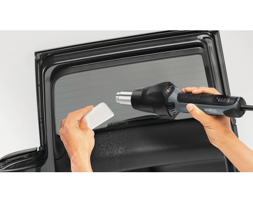 Außenaufnahme einer Autoscheibe mit Folie, die mit einem Heißluftfön und einem Rakel bearbeitet wird.