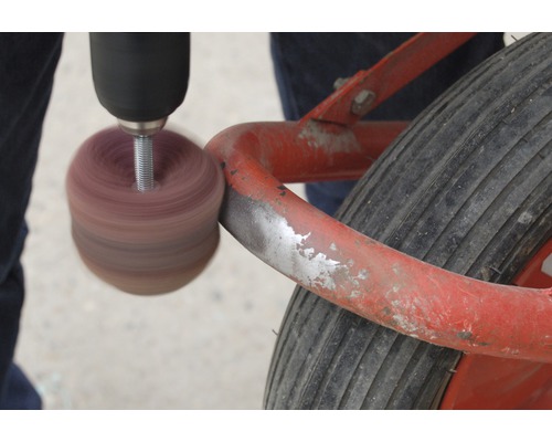 Eine Bohrmaschine mit Polieraufsatz schleift einen Bollerwagen.