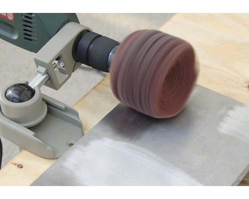 Eine Schleifmop-Bürste wird an einer Bohrmaschine befestigt, um eine Metalloberfläche zu schleifen.