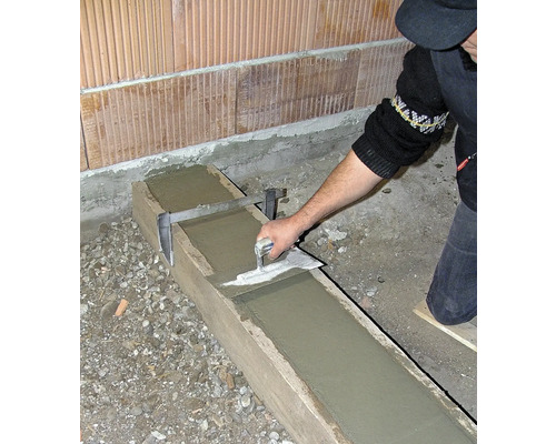 Eine Person glättet Beton in einer Holzschalung mit einer Glättkelle.