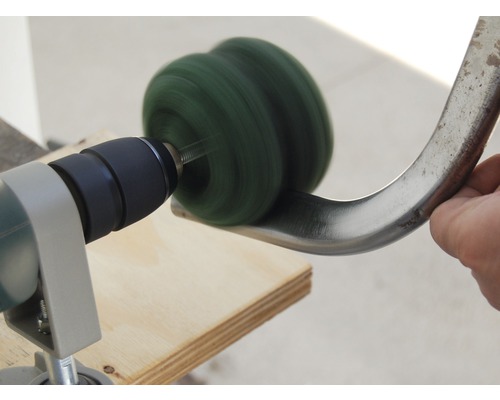 Eine Bohrmaschine mit Polieraufsatz schleift ein Metallobjekt.