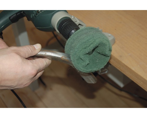 Eine Person benutzt eine Bohrmaschine mit Schleifaufsatz, um ein Metallstück zu bearbeiten.