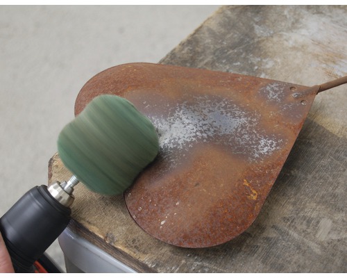 Eine Bohrmaschine mit Schleifscheibe reinigt eine rostige Metallschaufel.