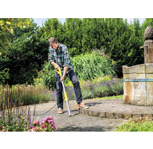 Un homme enlève les mauvaises herbes avec un scarificateur électrique sur une surface pavée du jardin.