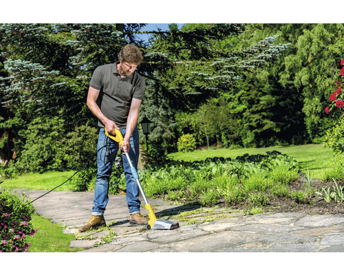 Un homme utilise une brosse électrique pour nettoyer les pavés dans le jardin.