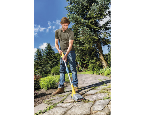 Un homme utilise un nettoyeur de joints sur un chemin pavé dans le jardin pour enlever les mauvaises herbes.
