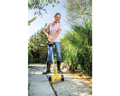 Eine Frau benutzt einen elektrischen Fugenreiniger, um Unkraut zwischen Pflastersteinen zu entfernen.