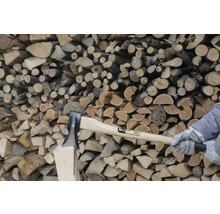 Hacher du bois avec une hache devant une pile de bois.