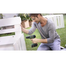Homme portant des lunettes de sécurité utilisant une perceuse pour assembler une étagère en bois blanc dans le jardin. Logo Bosch.