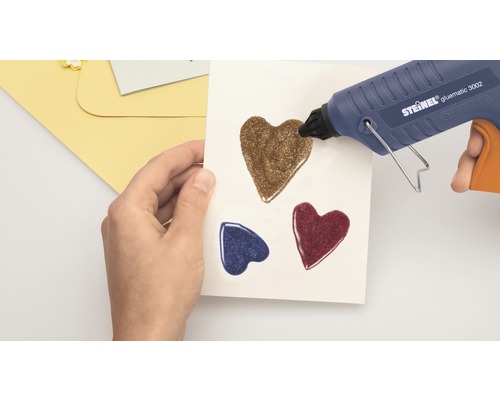Pistolet à colle chaude appliquant des coeurs pailletés sur du papier