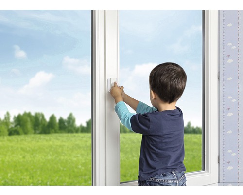Garçon actionnant une poignée de fenêtre avec sécurité enfant sur une fenêtre blanche