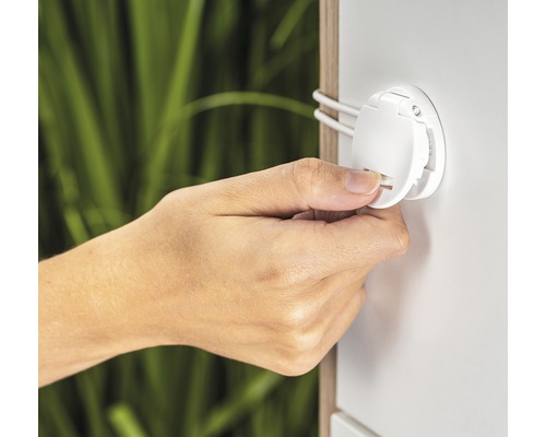 Hand betätigt eine weiße Schranksicherung zur Kindersicherung