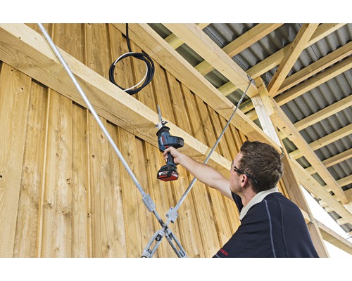 Un homme coupe du métal avec une scie sabre sans fil dans un bâtiment en bois