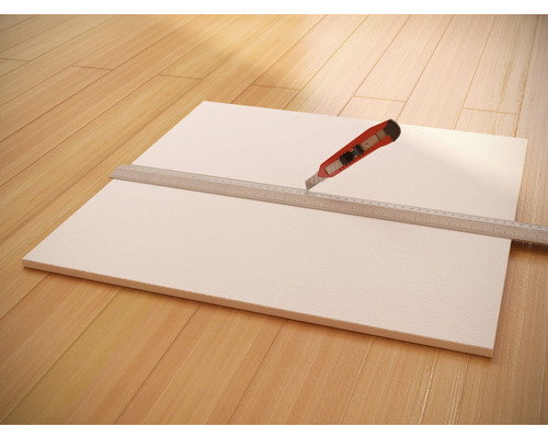 Eine Dämmplatte wird mit einem Cuttermesser und einem Lineal zugeschnitten.