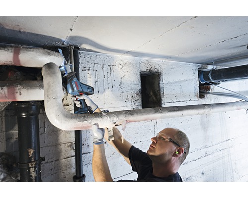 Un homme utilise une scie sabre pour couper un tuyau dans une cave.