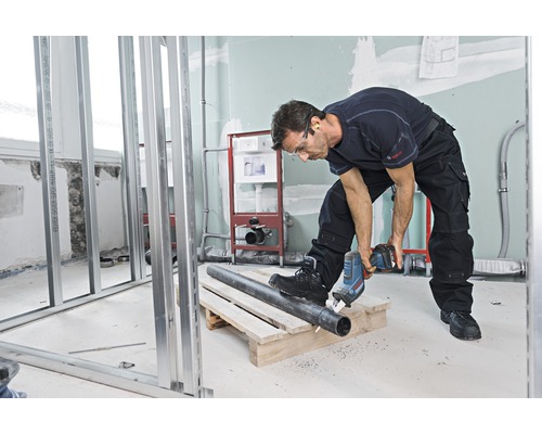 Un homme coupe un tuyau avec une scie sabre dans une salle de bains en construction.