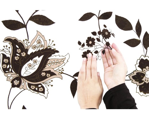 Une personne fixe une bordure autocollante marron à motifs floraux sur un mur blanc