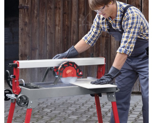 Ein Mann mit Schutzbrille und Handschuhen bedient eine Fliesenschneidmaschine, um eine Fliese zu schneiden.