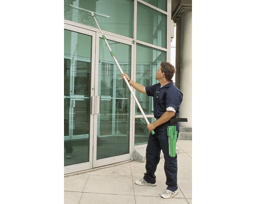 Un homme nettoie une porte vitrée avec un lave-vitre télescopique.