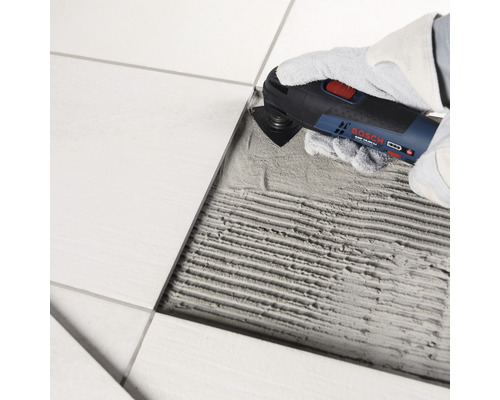 Eine Person entfernt mit einem Multifunktionswerkzeug eine Fliese.