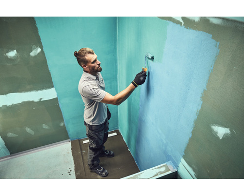 Artisan appliquant un joint avec un rouleau de peinture dans la salle de bains