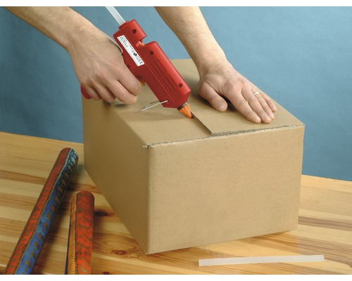 Eine Person benutzt eine Heißklebepistole, um einen Karton zu verschließen.