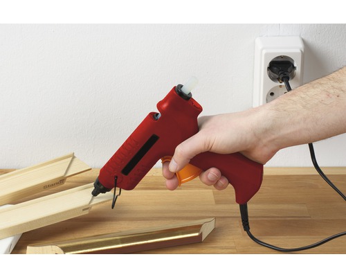 Eine Hand hält eine Heißklebepistole, um einen Holzrahmen zusammenzukleben.