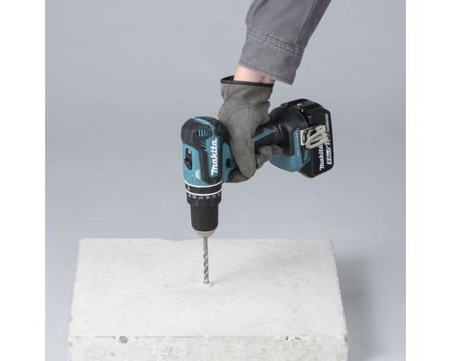 Une main gantée perce un bloc de béton avec une perceuse-visseuse sans fil.