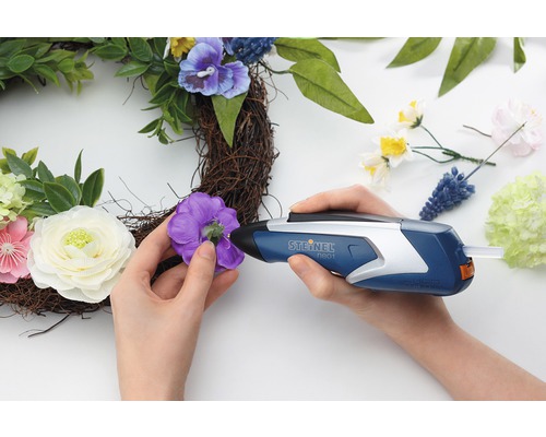 Person befestigt mit einer Heissklebepistole eine Blume an einem Kranz.