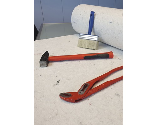 Hammer, Farbroller, Quast und Rohrzange liegen auf dem Untergrund.