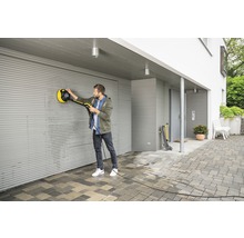 Un homme nettoie une porte de garage enroulable avec une brosse rotative d''un nettoyeur haute pression