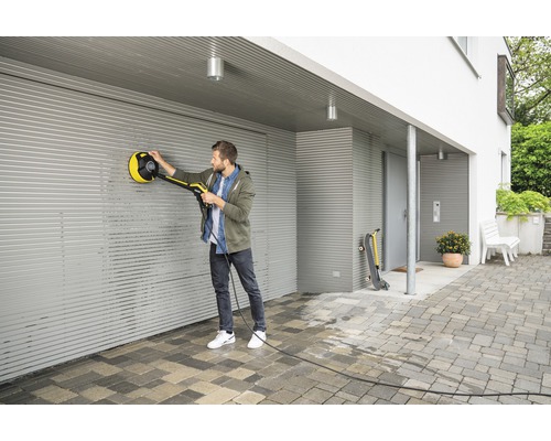 Un homme nettoie une porte de garage enroulable avec une brosse rotative d''un nettoyeur haute pression