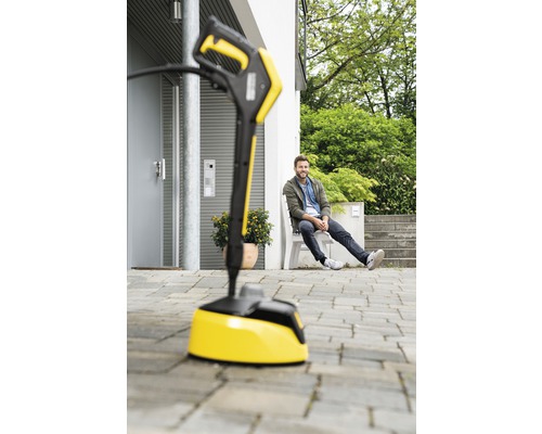 Nettoyeur de surfaces jaune devant une maison avec un homme assis