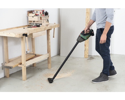 Un homme aspire des copeaux de bois avec un aspirateur sans fil à côté d''un établi.