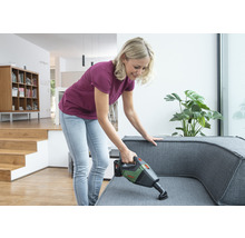 Femme aspire le canapé avec un aspirateur à main sans fil dans un appartement lumineux
