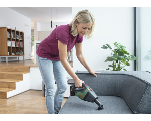 Femme aspire le canapé avec un aspirateur à main sans fil dans un appartement lumineux