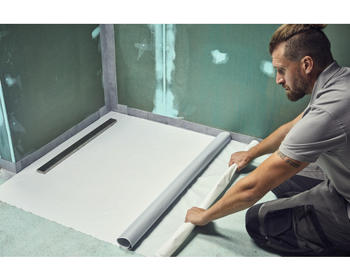 Un homme pose une membrane d''étanchéité dans la salle de bains