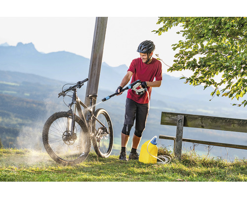 Ein Mann reinigt ein Fahrrad mit einem mobilen Hochdruckreiniger im Freien.