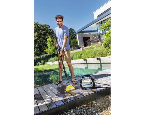 Ein Mann reinigt eine Holzterrasse mit einem Hochdruckreiniger neben einem Pool