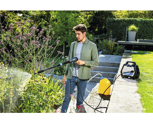 Un homme utilise un nettoyeur haute pression dans le jardin pour arroser les plantes.