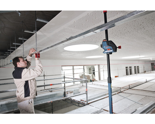 Un homme monte une construction de plafond avec un laser lignes croisées et un trépied de plafond dans une pièce.