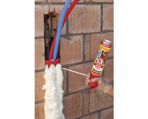 Ausfüllen eines Lochs in einer Ziegelwand mit Bauschaum um Rohre herum