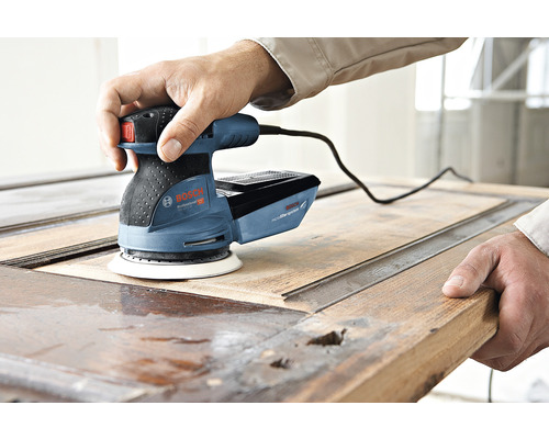 Ein Mann benutzt einen Bosch Exzenterschleifer, um eine Holztür abzuschleifen.