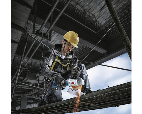 Ein Bauarbeiter mit Schutzhelm benutzt einen Winkelschleifer auf einem Gerüst.
