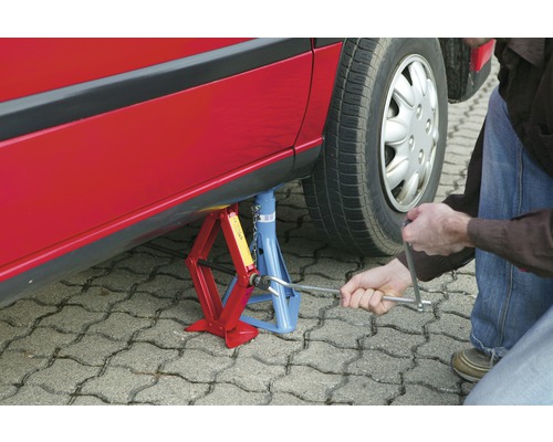 Ein rotes Auto, das mit einem Wagenheber und Unterstellbock angehoben wird, während eine Person mit einem Radkreuz hantiert.